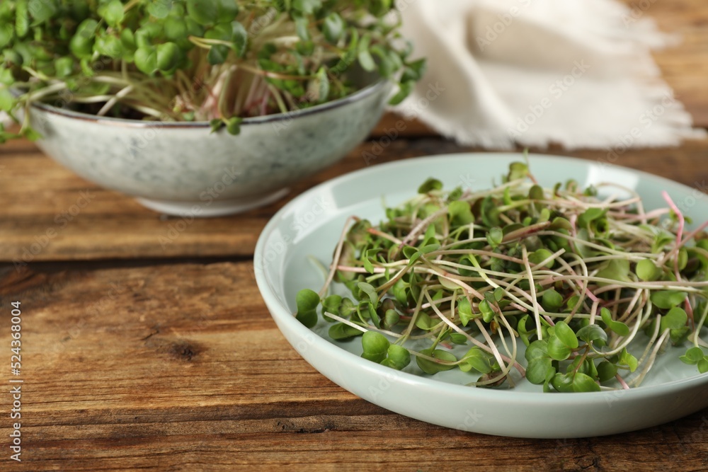 Plate with fresh radish microgreens on wooden table, space for text Plate with fresh radish microgreens on wooden table, space for text