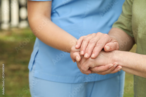 Elderly woman and female caregiver holding hands outdoors, closeup