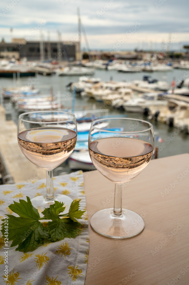 Obraz premium Rose wine in glasses served on outdoor terrace with view on old fisherman's harbour with colourful boats in Cassis, Provence, France