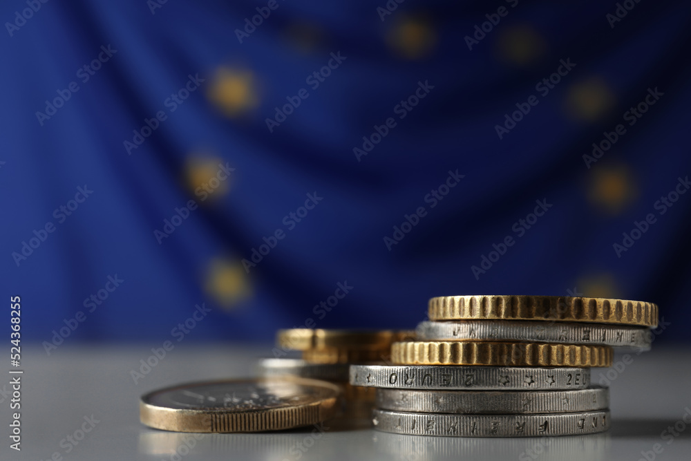 Many different coins on table against European Union flag, closeup. Space for text Many different coins on table against European Union flag, closeup. Space for text