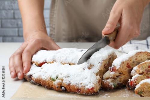 Woman cutting traditional Christmas Stollen with icing sugar at white wooden table, closeup