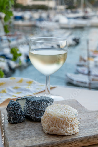 Pairing of French goat cheese crottin and glass of white French wine served with view on boats in harbor of Cassis, Provence, France photo