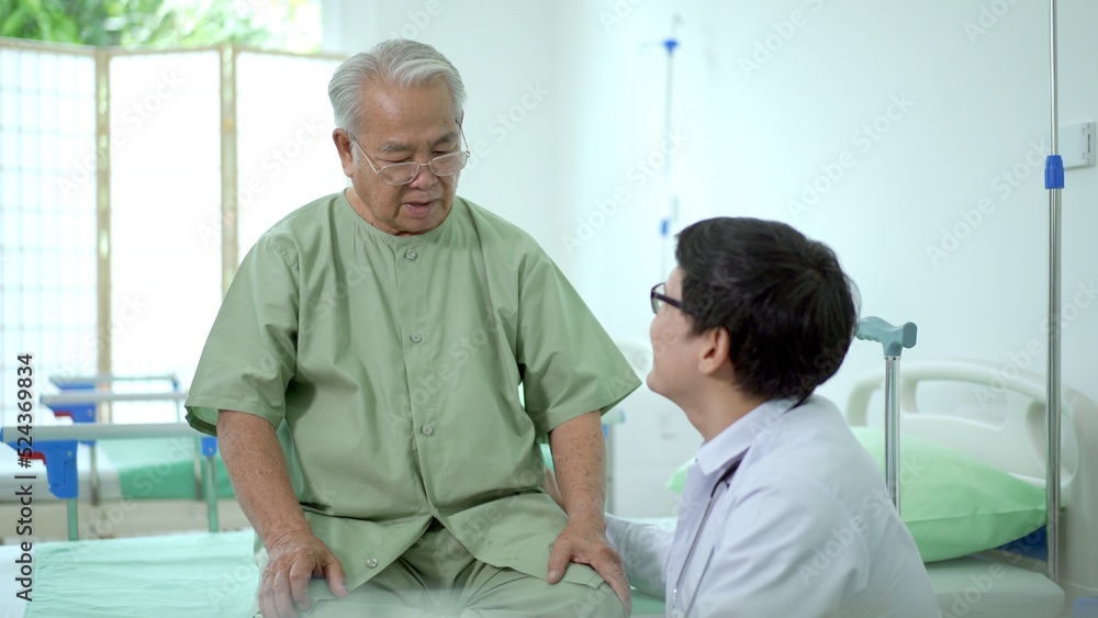 Fototapeta premium Elder Asian man sitting on the bed and talking to doctor about his physical injuries at his knee.