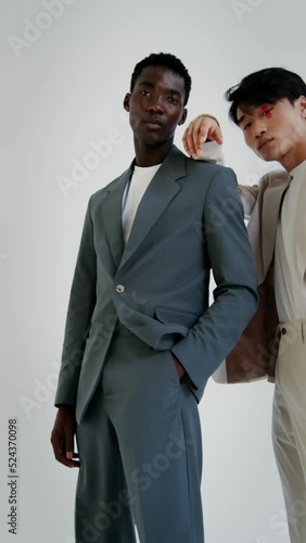 Two men in business suits posing on a white background, vertical video