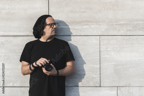 Caucasian male photographer with camera in hand looking to his left with gray background wall and copy space.  . photo