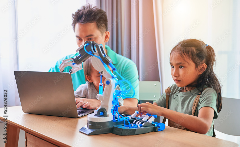 Asian father and two daughters playing with robotic arms and using a laptop. Asian father and two daughters playing with robotic arms and using a laptop.
