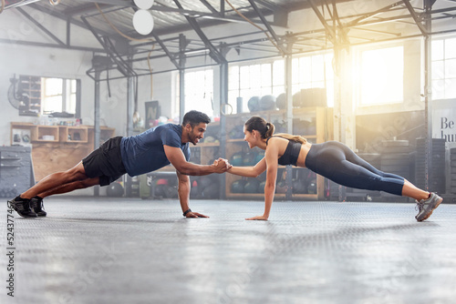 Active couple holding hands for support in pushup, plank and balance training during fitness, workout and exercise in a gym. Sporty, strong and fit athletes helping with bodyweight wellness challenge photo