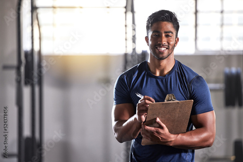 Gym, workout and personal trainer with clipboard consulting at a training sports in gym. Portrait of muscular, active and smiling fitness coach writing on health, wellness and exercise with flare
