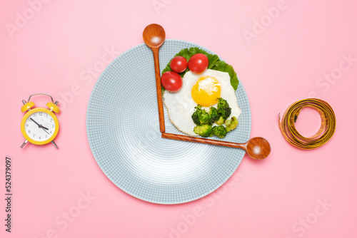 Plate with healthy food, wooden spoons and measuring tape on pink background top view, intermittent fasting concept.
