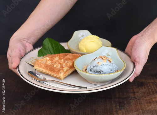 Hands holding dish with organic ice cream and Belgium waffles on wooden table background 
