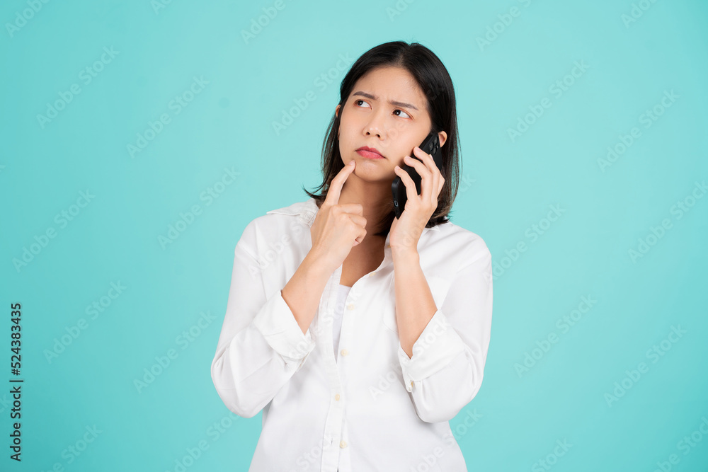 Portrait of young asian woman wearing white T-shirt on green background with dreamy look, thinking while holding smartphone. Tries to write up a message. Portrait of young asian woman wearing white T-shirt on green background with dreamy look, thinking while holding smartphone. Tries to write up a message.