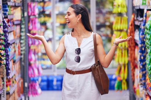 Shopping, store and retail with a young woman customer at a supermarket or shop with products in the background. Money, buying and spending by a female consumer looking happy with options and variety photo