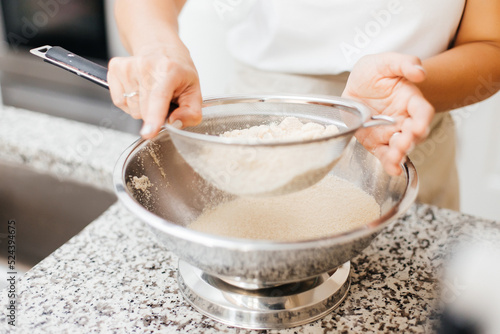 A young beautiful woman cooks in a bright kitchen. Cooking macaroons. A cute girlp repares dough for cakes, hands and ingrident closeup. Cooking macaroons. Cookie baking