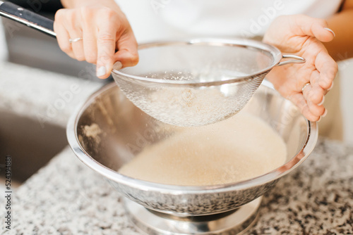 A young beautiful woman cooks in a bright kitchen. Cooking macaroons. A cute girlp repares dough for cakes, hands and ingrident closeup. Cooking macaroons. Cookie baking photo