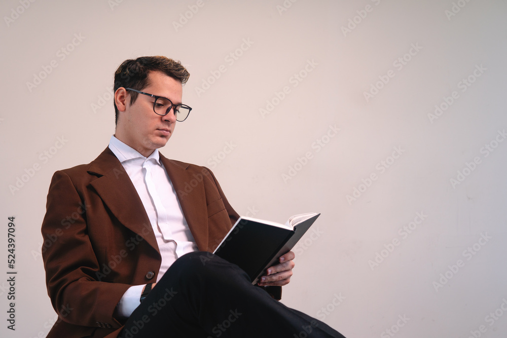 Intellectual man dressed in a suit and glasses reading book sitting on a white background. Elegant business man reading his book. University professor with a book in his hands. High quality photo Intellectual man dressed in a suit and glasses reading book sitting on a white background. Elegant business man reading his book. University professor with a book in his hands. High quality photo