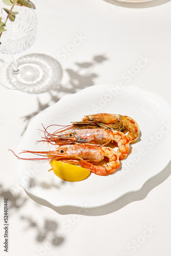 Grilled shrimps on light background with shadows. Grilled prawns with lemon on white table. Aesthetic composition with bbq shrimps. Bbq prawns. Grilled seafood. Summer menu.