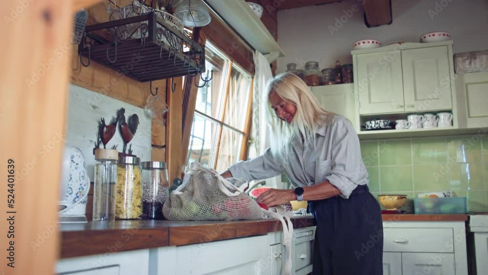 Senior woman unpacking local food in zero waste packaging from bag in kitchen at home. Senior woman unpacking local food in zero waste packaging from bag in kitchen at home.