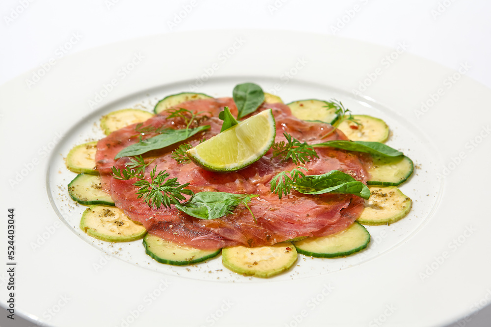Beef carpaccio with zucchini and cucumber on white table with sunlight shadows. Appetizer of meat - beef carpaccio on summer dining. Sliced raw meat in italian style. Aesthetic menu. Beef carpaccio with zucchini and cucumber on white table with sunlight shadows. Appetizer of meat - beef carpaccio on summer dining. Sliced raw meat in italian style. Aesthetic menu.