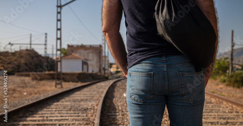 Rear view of adult man in jeans carrying bag walking on railway track