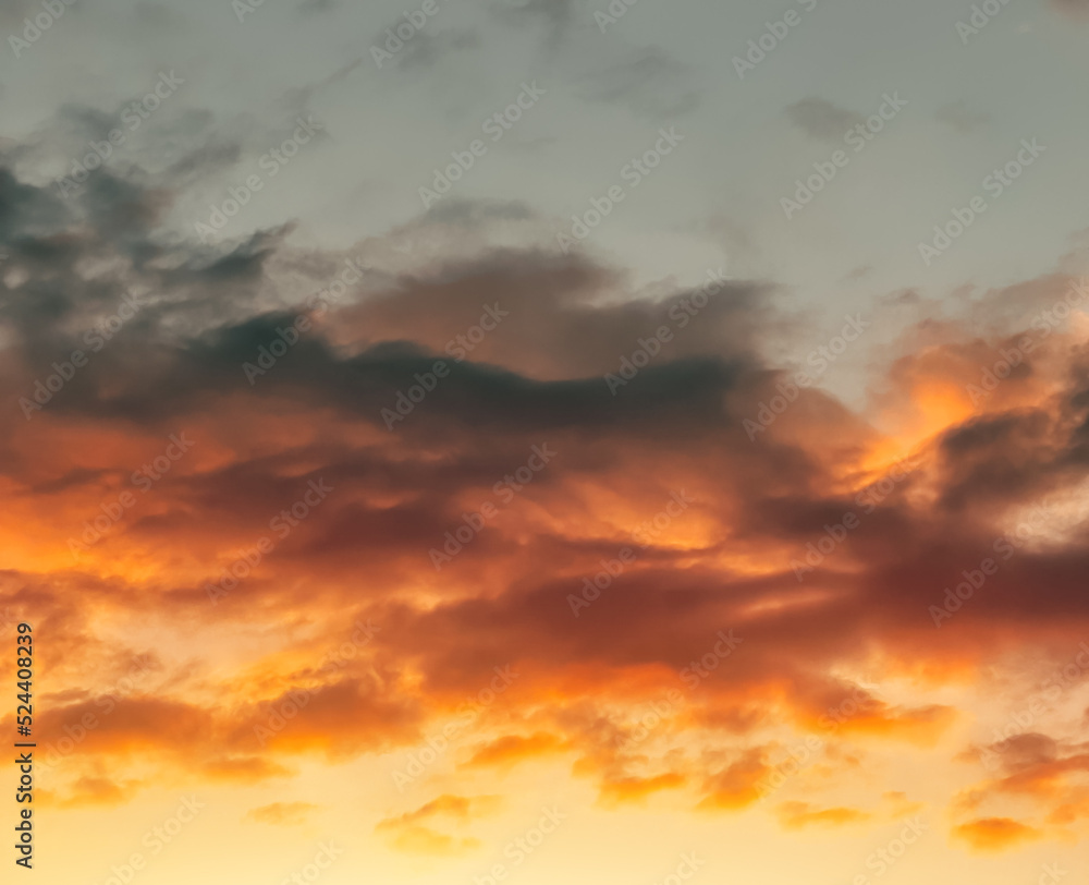 Dramatic sunset landscape with puffy clouds lit by orange setting sun and blue sky.