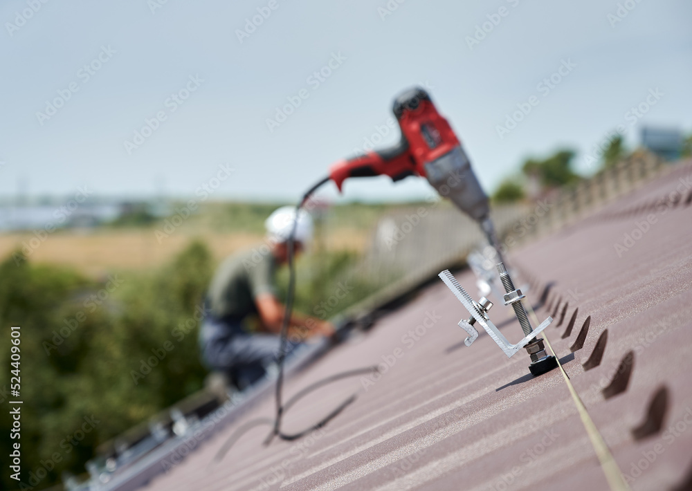 Close up of clamp. Worker prepearing to installation photovoltaic solar panel system on the roof of house. Man and electric screwdriver on blurred background.
