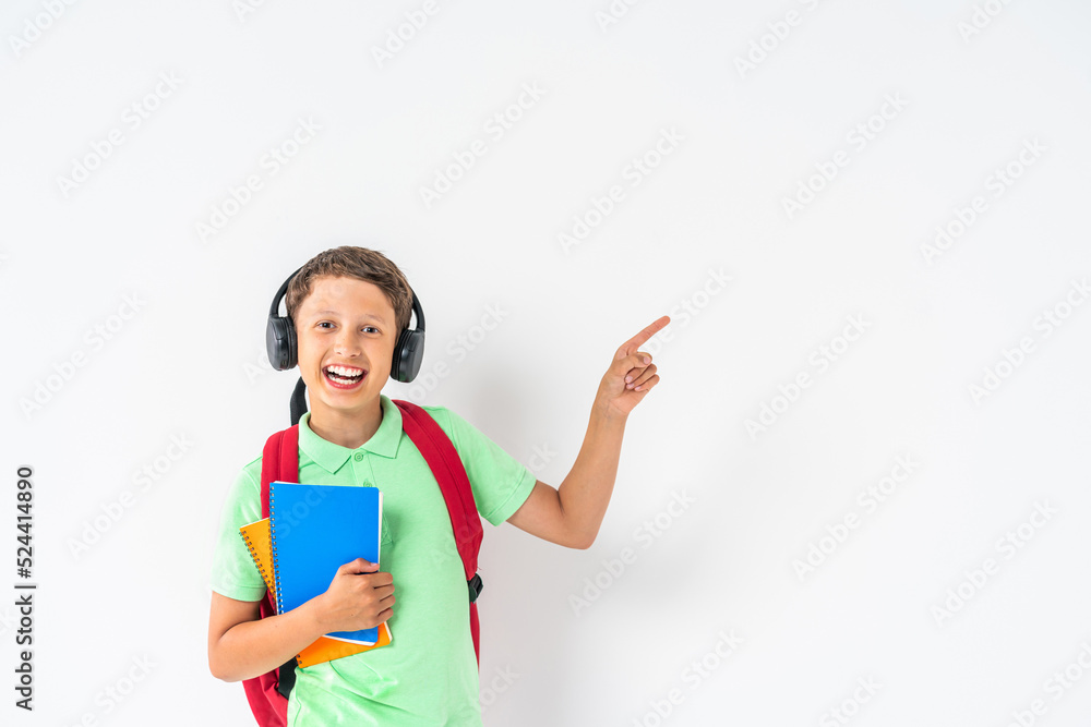 E-learning at school. A happy student wearing headphones with a tablet computer in his hands, points his finger at the copy space. Recommending remote online school on white background in the studio. E-learning at school. A happy student wearing headphones with a tablet computer in his hands, points his finger at the copy space. Recommending remote online school on white background in the studio.