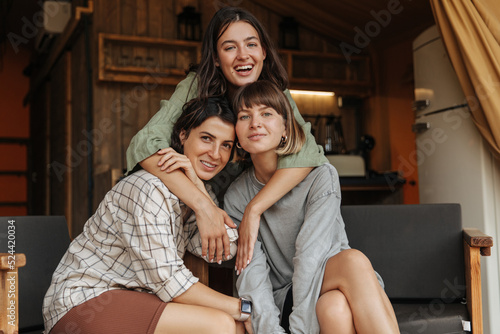 Friendly young caucasian girls look at camera, hugging sitting in country house on weekend. Brunettes wear casual clothes spring. Relaxation concept