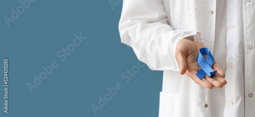 Doctor holding blue ribbon on color background with space for text, closeup. Prostate cancer awareness concept