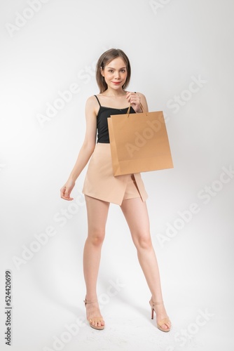 Full length body portrait of a young beautiful asian female executive lady wearing stylish modern attire with skirt holding a brown color shopping paper bag elegantly cheerful and cool stylish