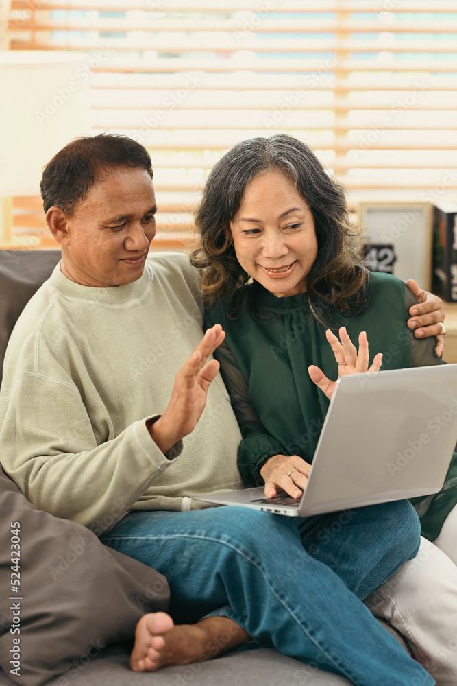 Happy retired couple making video call with family or friends on laptop while spending time together at home Happy retired couple making video call with family or friends on laptop while spending time together at home