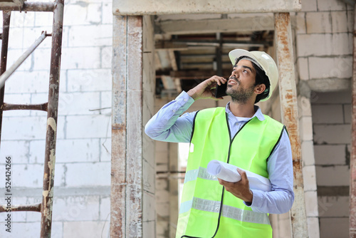 Technician civil engineer or specialist inspector discussing, brainstorm and planing real estate project work with smart mobile phone and blueprint at Industrial building site. Construction concept