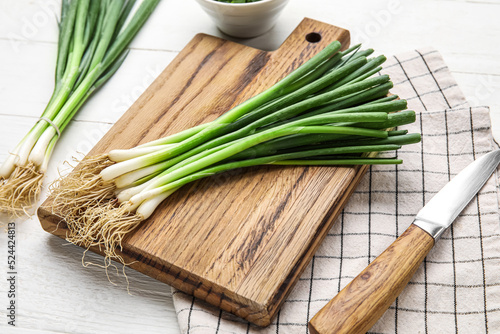 Board with bunch of fresh green onion on light wooden background  closeup