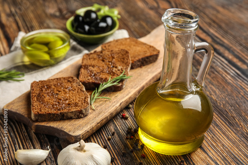 Decanter with fresh olive oil and bread on wooden table, closeup
