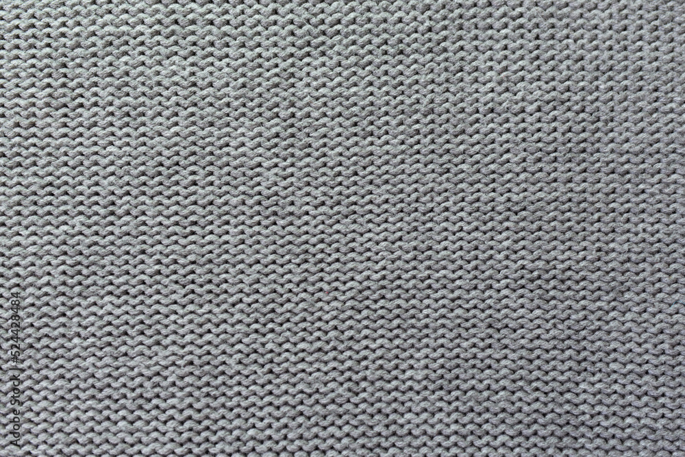 Knitted gray pattern closeup. Soft sweater texture, detailed yarn background. Natural woolen fabric, a fragment of a jersey pullover. Trendy backdrop for print, web design.