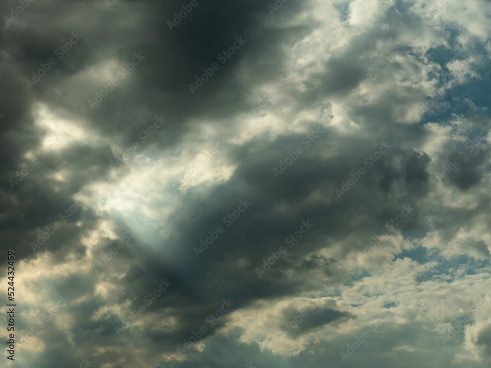 Pokryte szarymi chmurami niebo. Między chmurami znajdują się przerwy przez które można dostrzec błękit nieba i przedzierają się smugi światła. - obrazy, fototapety, plakaty 