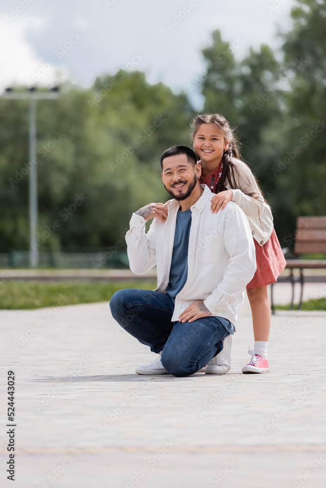 Smiling asian child hugging tattooed father in park. Smiling asian child hugging tattooed father in park.
