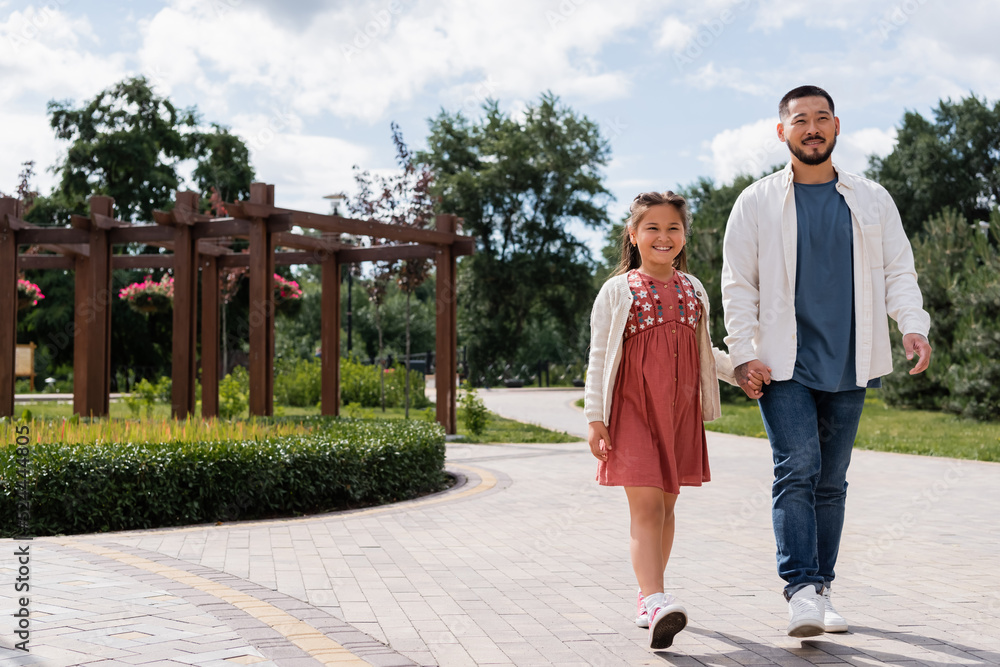 Fototapeta premium Asian dad and daughter walking in summer park.