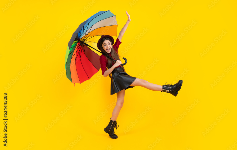 Excited teenager, glad amazed and overjoyed emotions. Teen girl under rainbow umbrella in autumn weather isolated on yellow background. Autumn kids clothes.