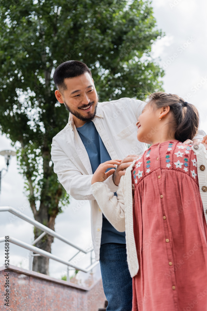 Low angle view of smiling asian dad looking at daughter in summer park. Low angle view of smiling asian dad looking at daughter in summer park.