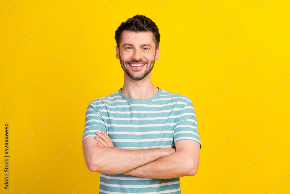 Portrait of young attractive man wear blue striped t-shirt hands folded genius influencer looking you isolated on yellow color background