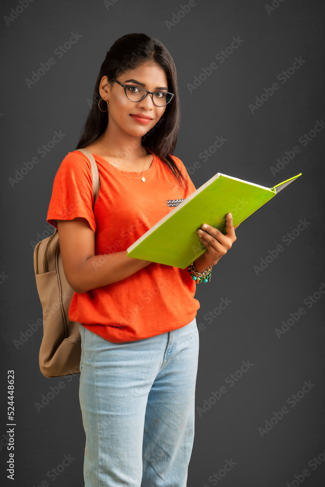 Beautiful young girl with a backpack standing and holding a notebook, posing on a grey background. Beautiful young girl with a backpack standing and holding a notebook, posing on a grey background.