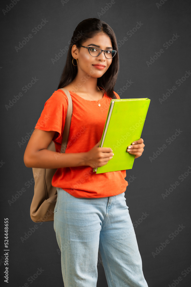 Beautiful young girl with a backpack standing and holding a notebook, posing on a grey background. Beautiful young girl with a backpack standing and holding a notebook, posing on a grey background.