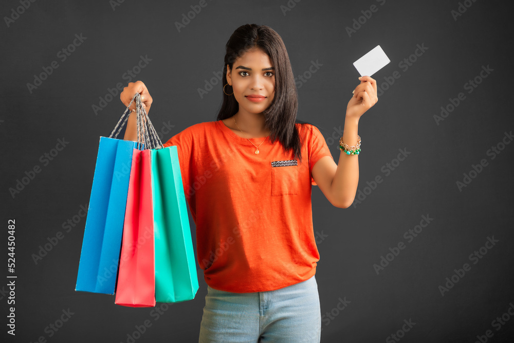 Beautiful young girl holding and posing with shopping bags and credit or debit card on a grey background Beautiful young girl holding and posing with shopping bags and credit or debit card on a grey background