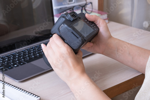 Studying online photography lessons. Female hands holding SLR camera at desktop with laptop