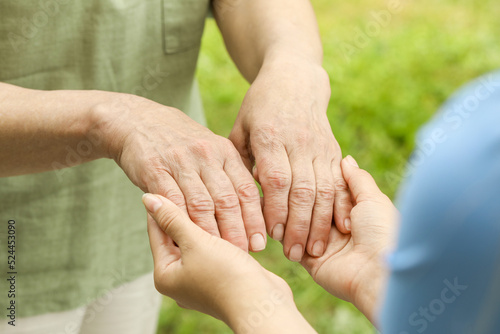 Elderly woman and female caregiver holding hands outdoors, closeup