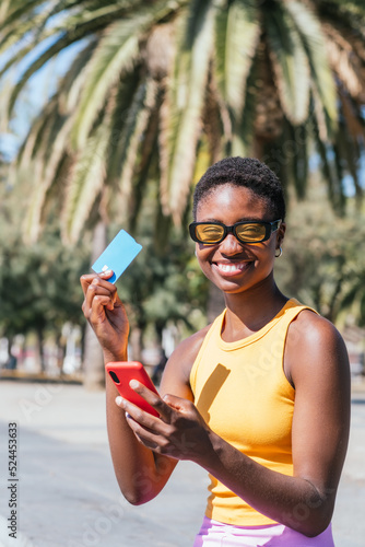 cheerful african woman showing her credit card while holding her phone. Concept of online shopping