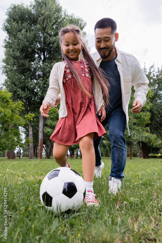 Wide angle view of cheerful preteen girl playing soccer with father in park.