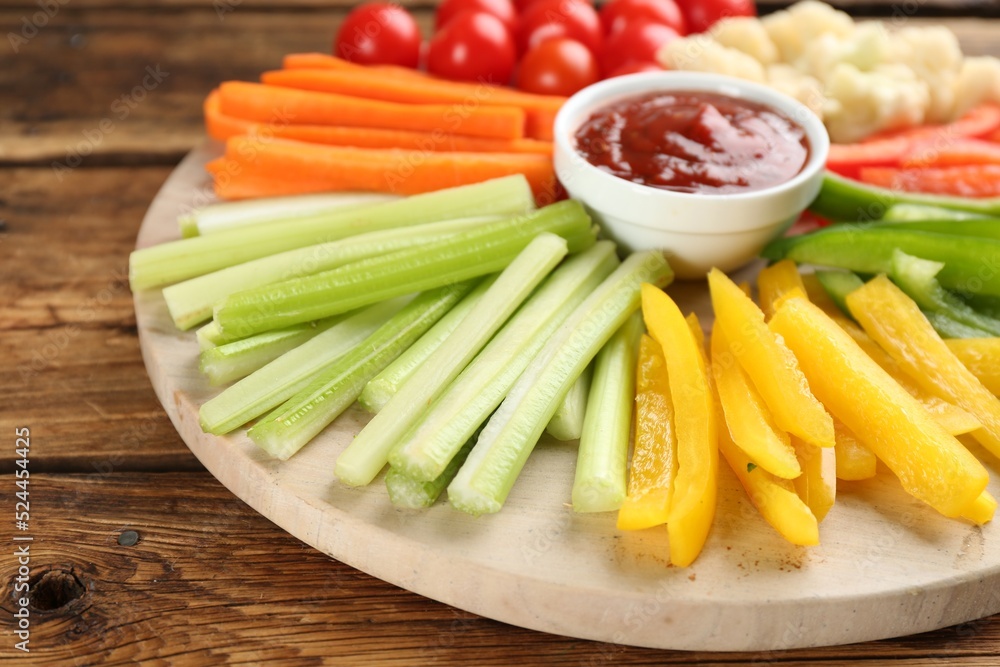 Board with celery sticks, other vegetables and dip sauce on wooden table, closeup