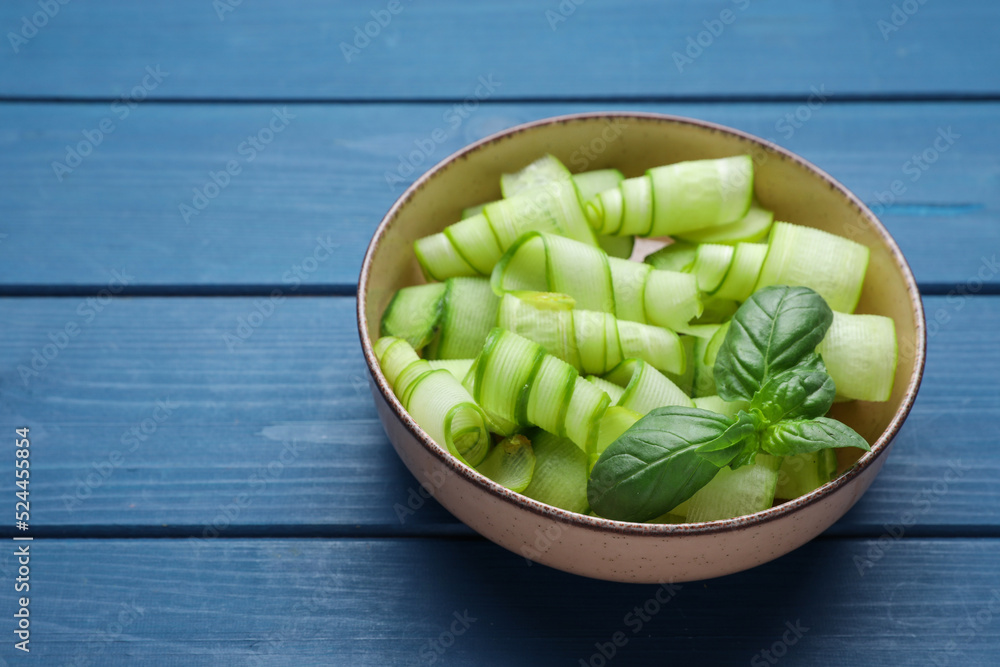 Slices of fresh ripe cucumber and basil in bowl on blue wooden table, space for text Slices of fresh ripe cucumber and basil in bowl on blue wooden table, space for text