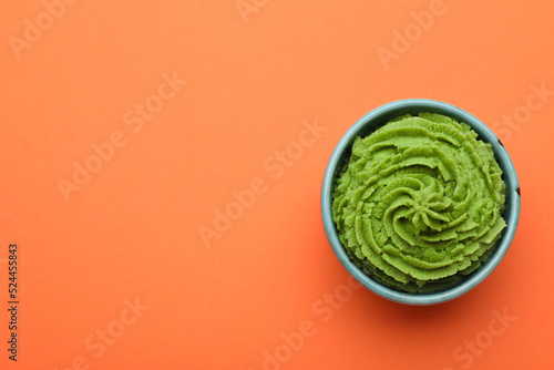 Bowl with swirl of wasabi paste on orange background  top view. Space for text